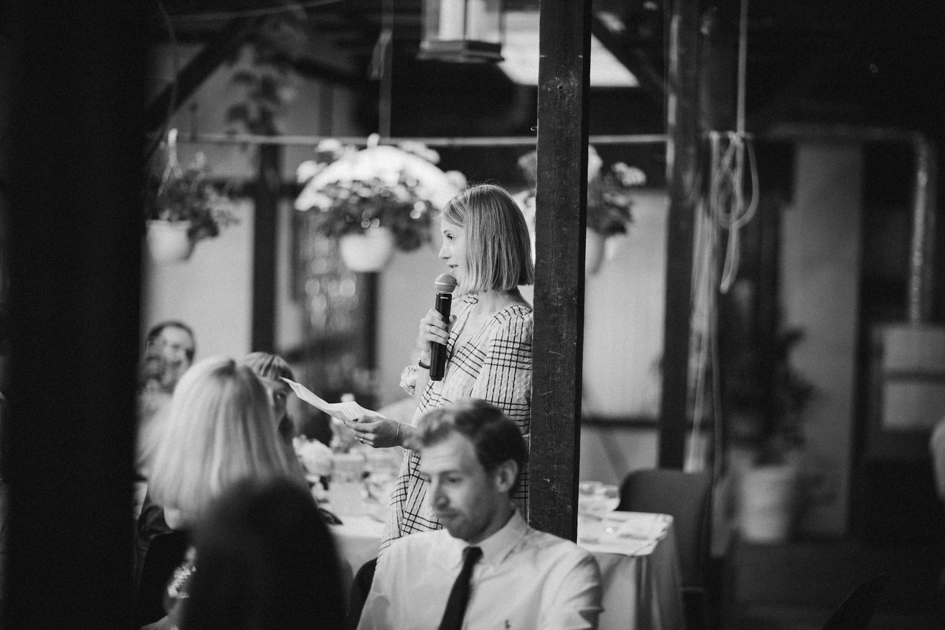 Renginio vedėjas su mikrofonu rankoje profesionaliai bendrauja su šventės svečiais šviesioje salėje.